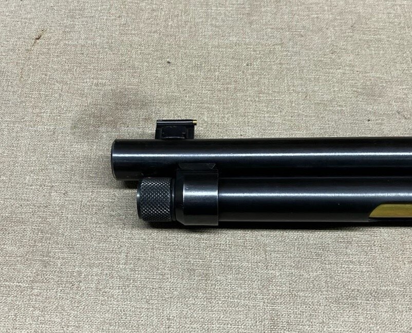 Muzzle of a tube-fed firearm before threading, with the front sight still installed and a full-length magazine cap nut