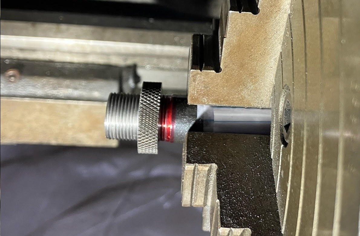 Shoulder-expanding collar in the lathe, attached with red Loctite, while a sacrificial knurled thread protector is in use