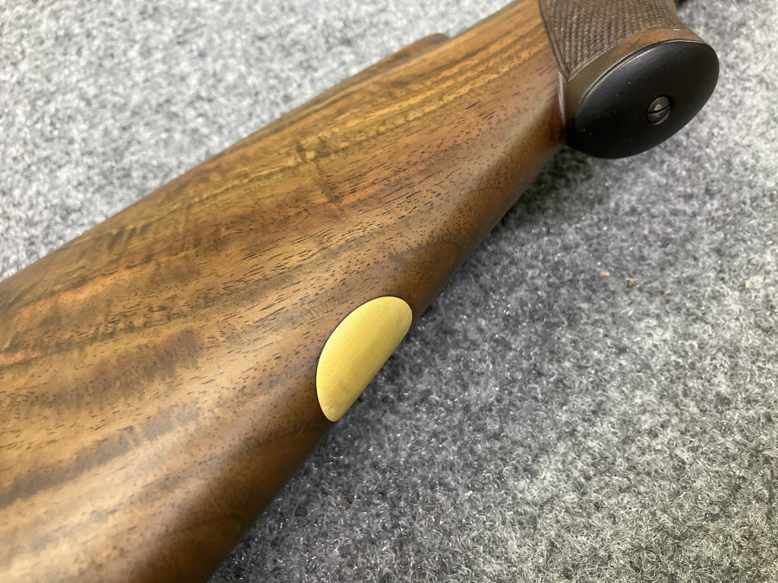 Brass medallion inlaid in the grip cap of a checkered walnut rifle stock